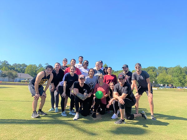 Allyon kickball team posing for a picture on a clear day with blue sky on a green field holding a kickball