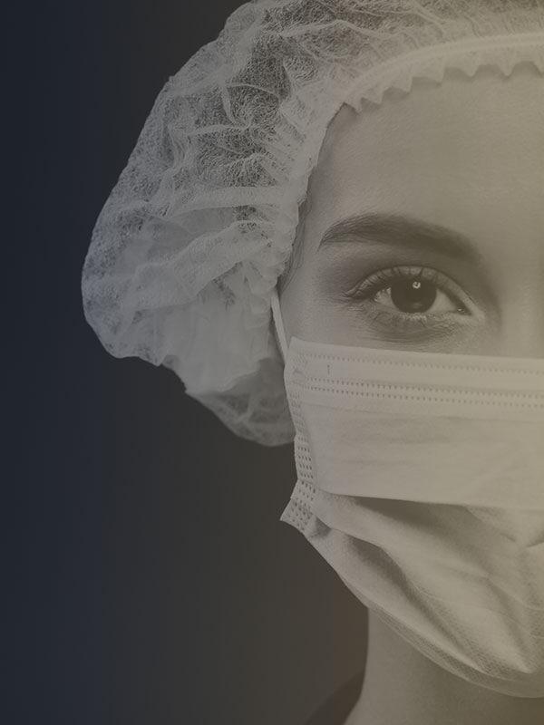 Allyon healthcare subcontractor wearing a mask and hair cover looking at the screen with a dark background